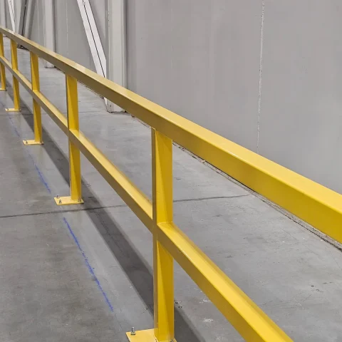 Run of yellow steel safety barriers bolted to a warehouse floor