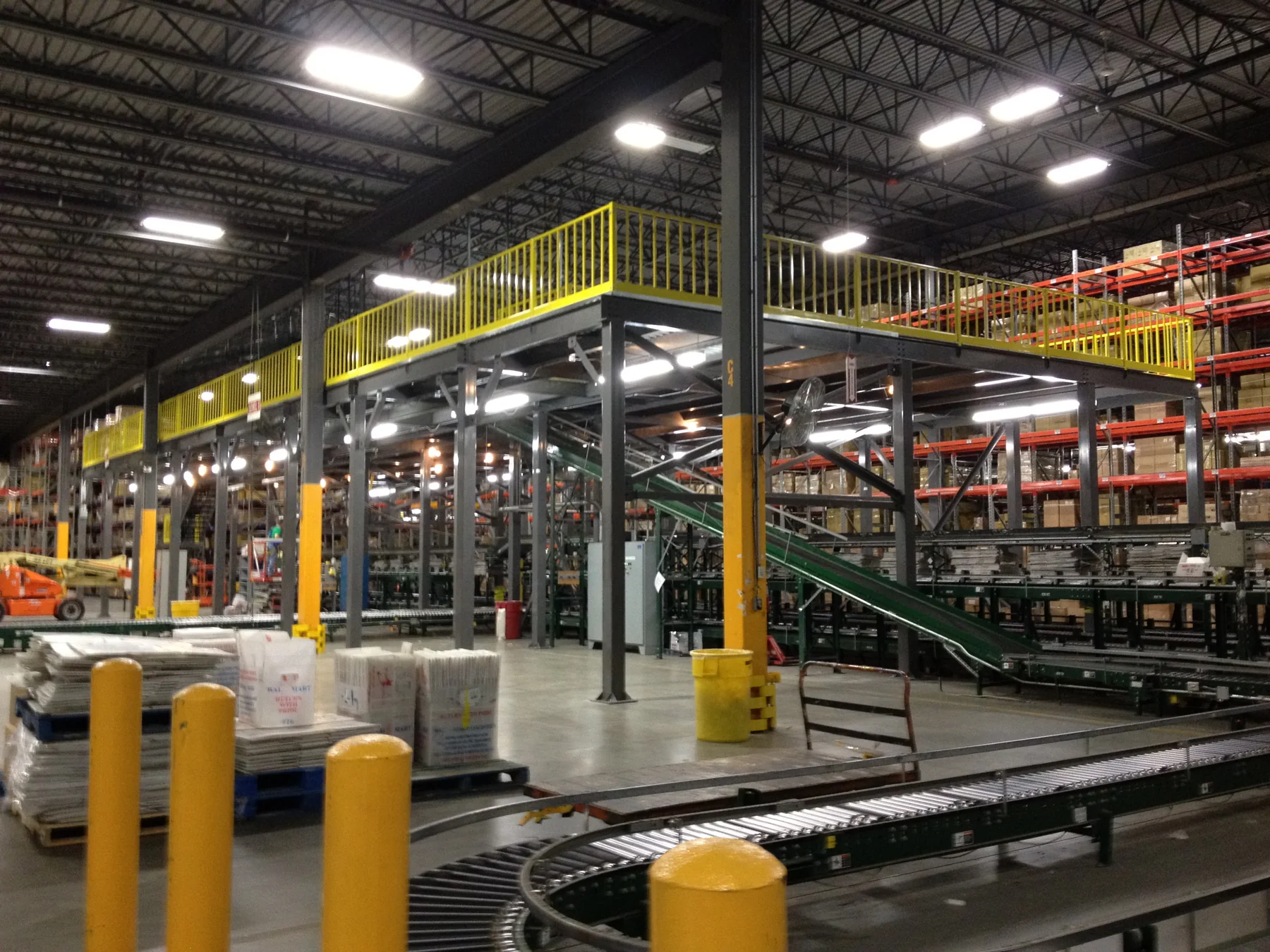 Structural warehouse mezzanine with yellow guardrails and operations beneath